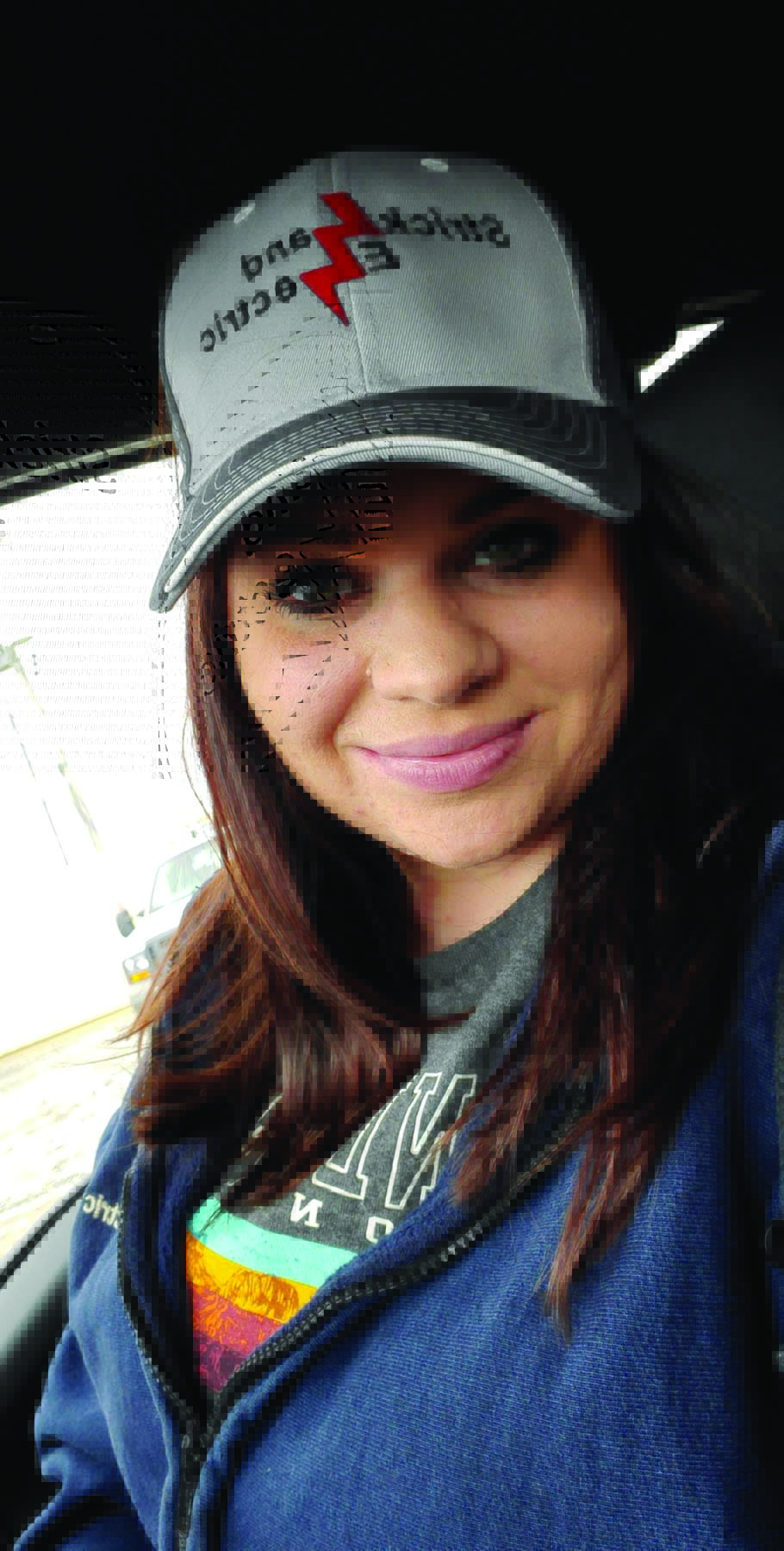 003_Abbey Strickland 4 A woman, Abbey Strickland, wears a Strickland Electric hat and smiles in a car. Image by Abbey Strickland.