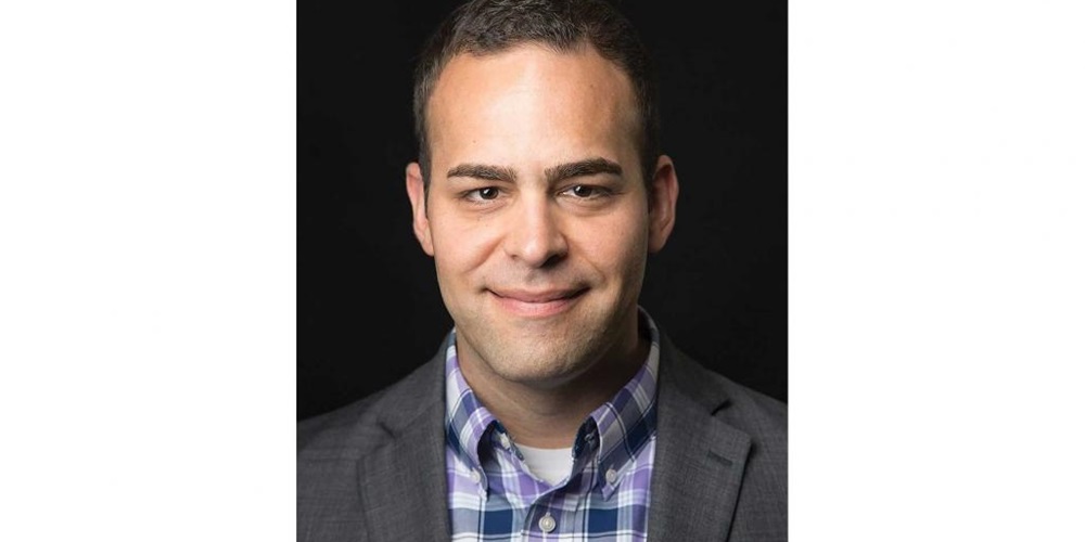 A man, Joe Kopko, smiles in front of a black background. Image by Aaron Siegel.