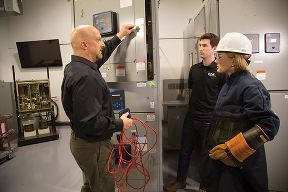 Two men and a women look at a switchgear box. One holds a long red wire. Image by Eaton.