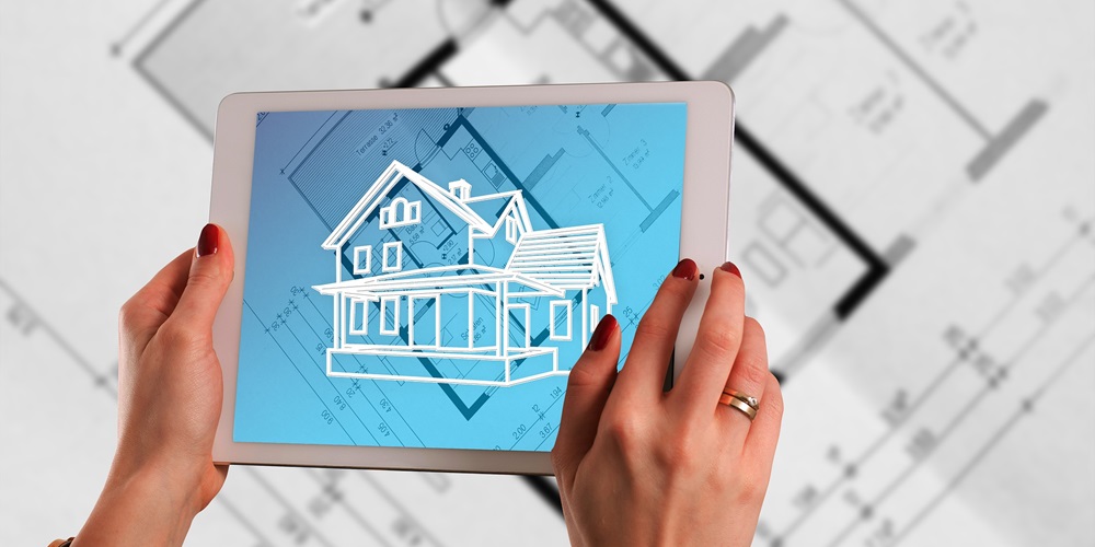 Two hands holding a tablet showing a building model, with printed building plans in the background