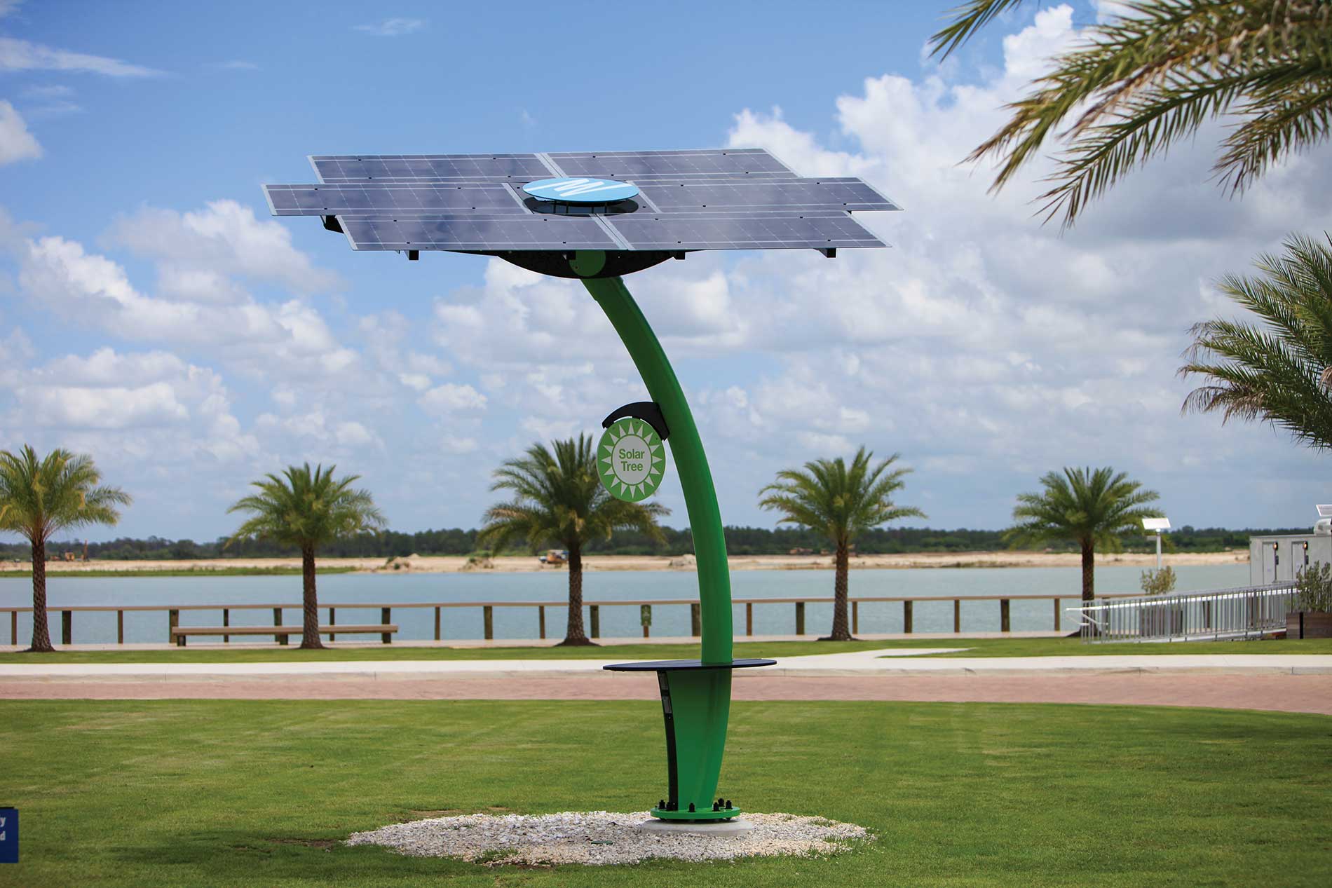 A green metal structure topped with a solar panel sits on a grass area next to a body of water. Image by Florida Power & Light Co. and Babcock Ranch.