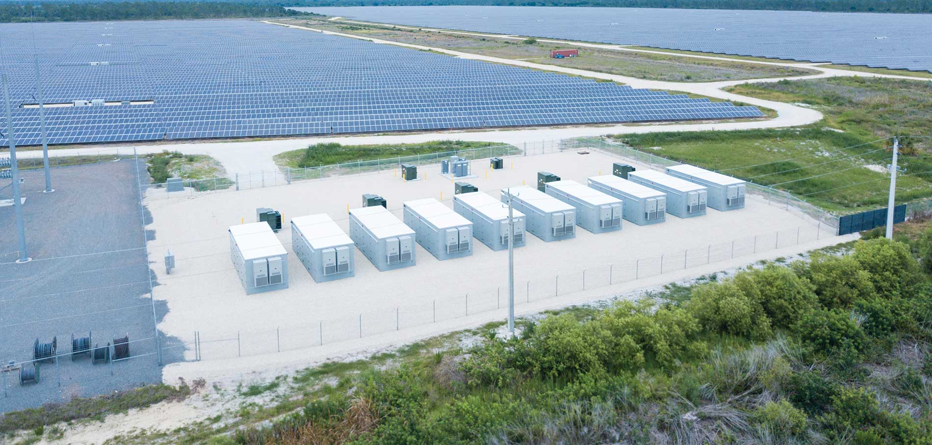 Several solar batteries next to a solar grid and body of water. Image by Florida Power & Light Co. and Babcock Ranch.