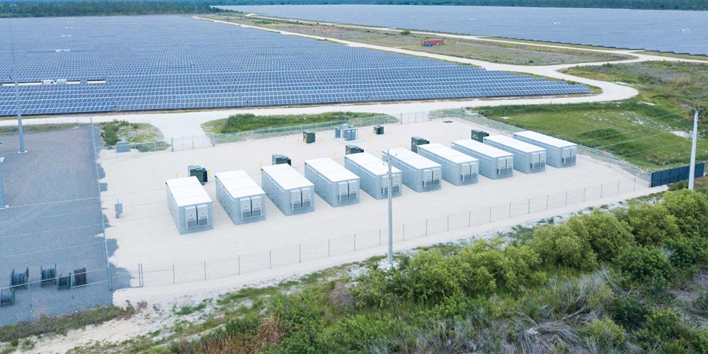 Several solar batteries next to a solar grid and body of water. Image by Florida Power & Light Co. and Babcock Ranch.