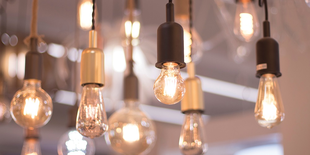 Various lightbulbs, turned on, hang from a ceiling