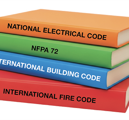 A stack of books labeled with various code names: National Electrical Code, NFPA 72, International Building Code and International Fire Code