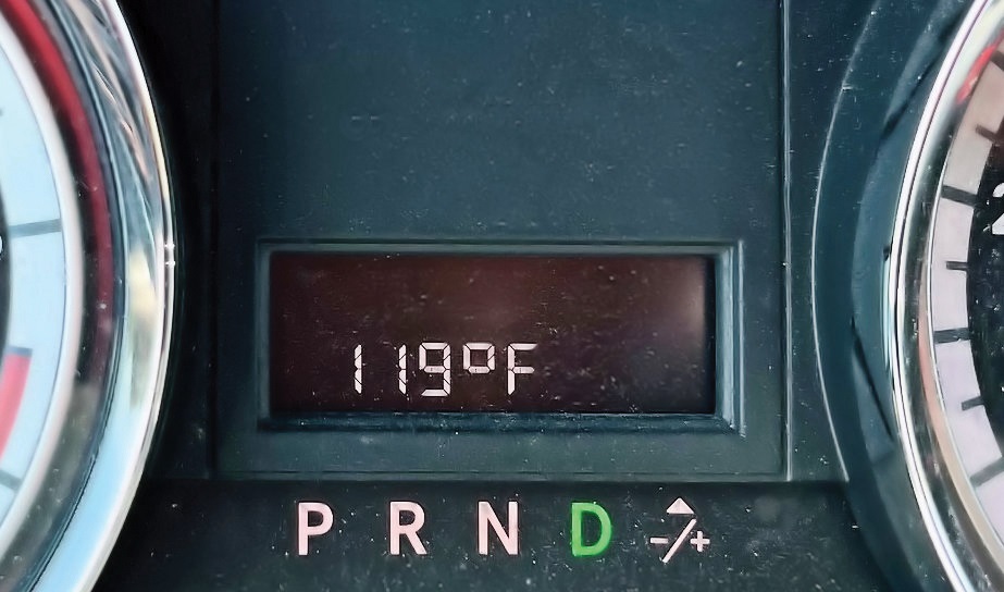 A car's dashboard shows the outside temperature at 119 degrees Fahrenheit. At least it’s a dry heat.