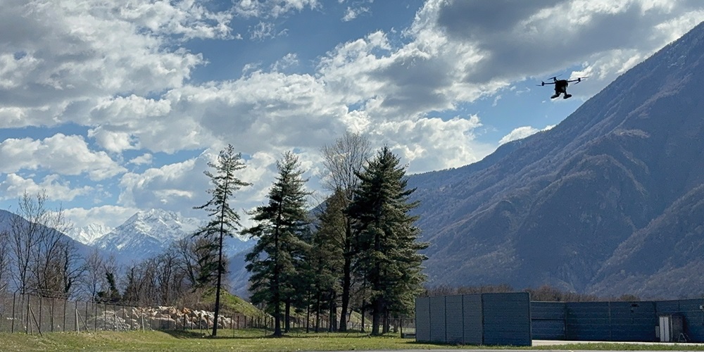 A drone flies over a remote utility site, with mountains in the background.