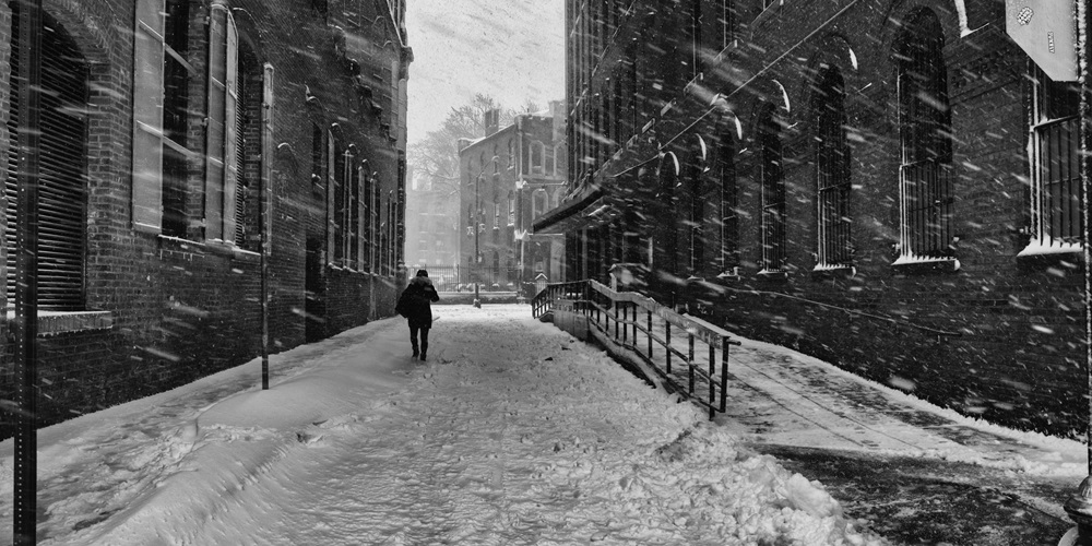 A person walks down an empty snow-covered street during a snow storm