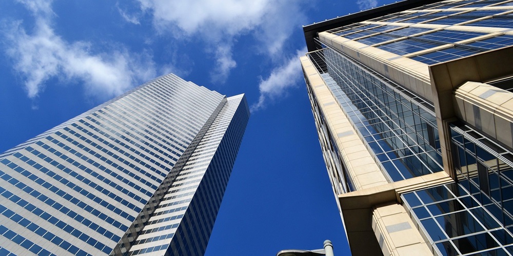 View of two skyscrapers against a blue sky and clouds, looking upwards from the ground