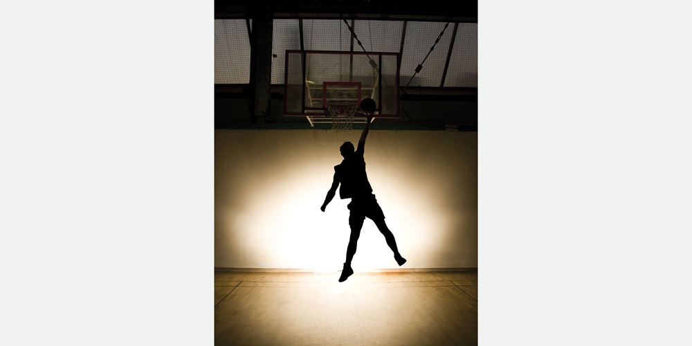 A backlit basketball player does a slam dunk | Shutterstock / S Pytel