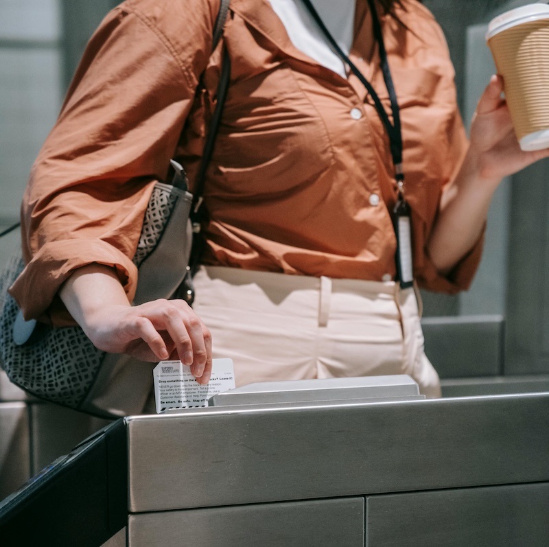 A woman holding a coffee and purse swipes her badge at an access control station