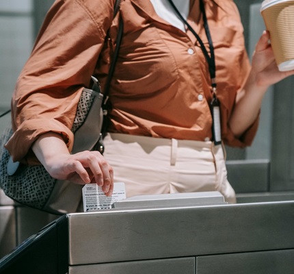 A woman holding a coffee and purse swipes her badge at an access control station