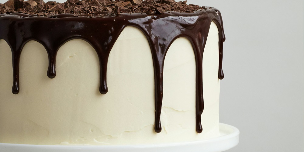 A cake with white frosted topped with chocolate drizzle.