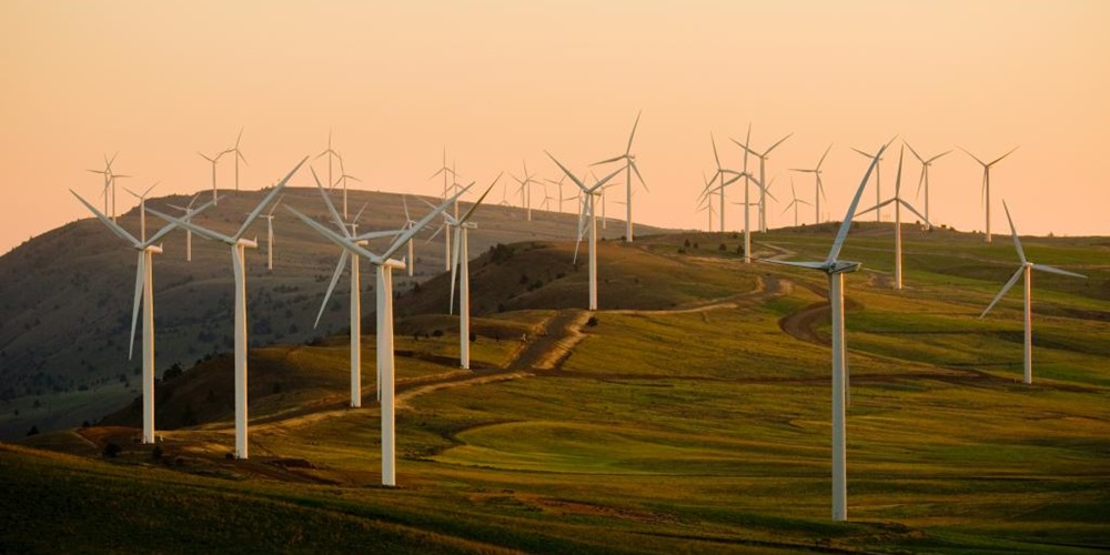 Wind turbine on green hills against an orange sky. Image by Unsplash.