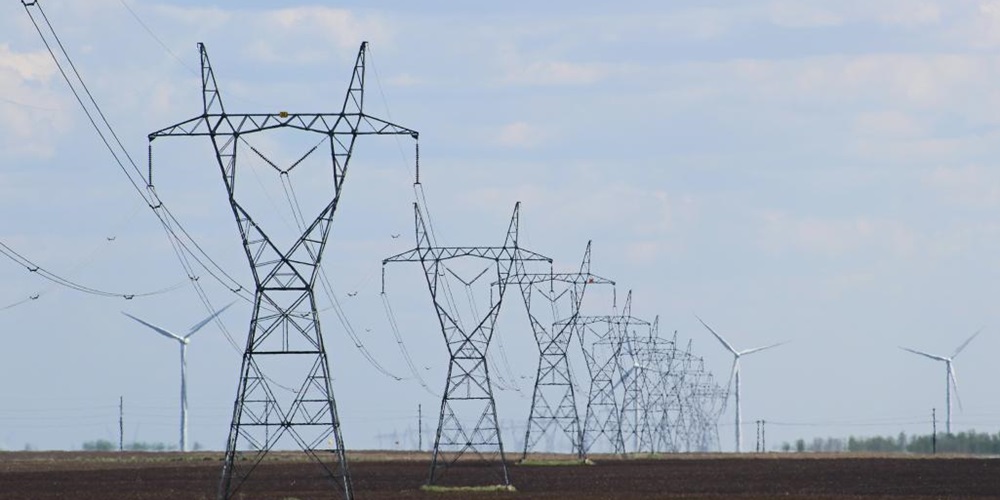 Transmission towers in fields against a blue sky. Image by Shutterstock.