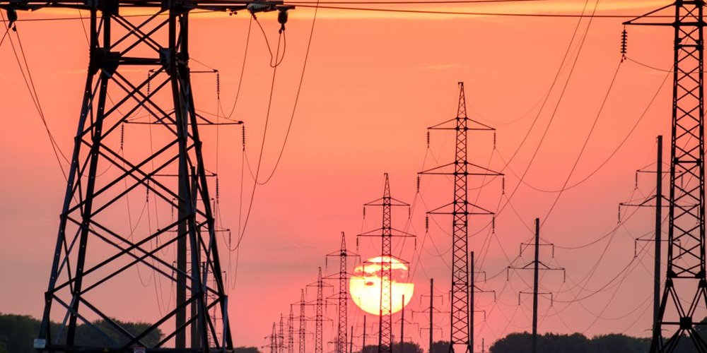 Power towers silhouetted against a setting sun. Image by Unsplash / Andrey Metelev.