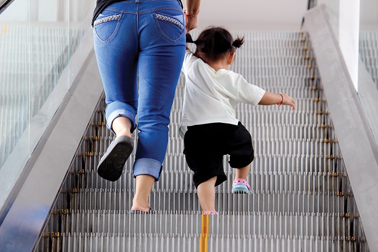 child and adult walking up escalator