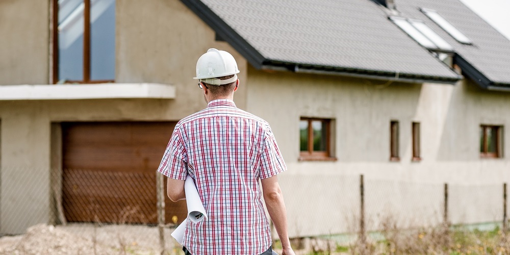 person standing in front of a house holding blueprints