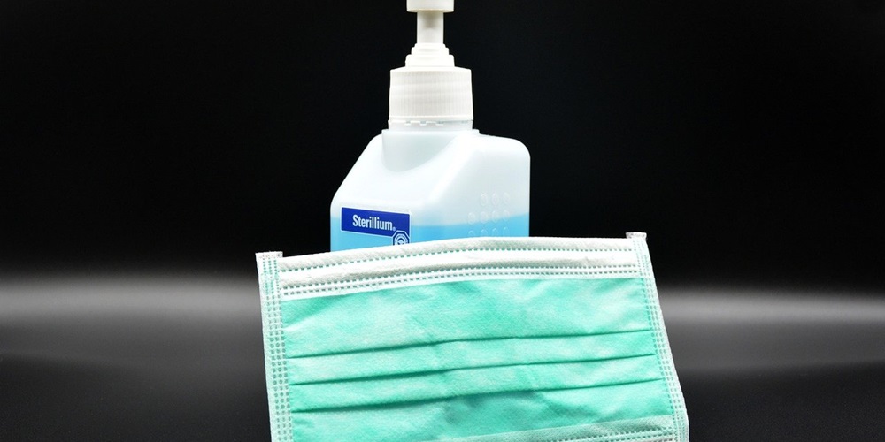 A bottle of hand sanitizer behind a disposable face mask