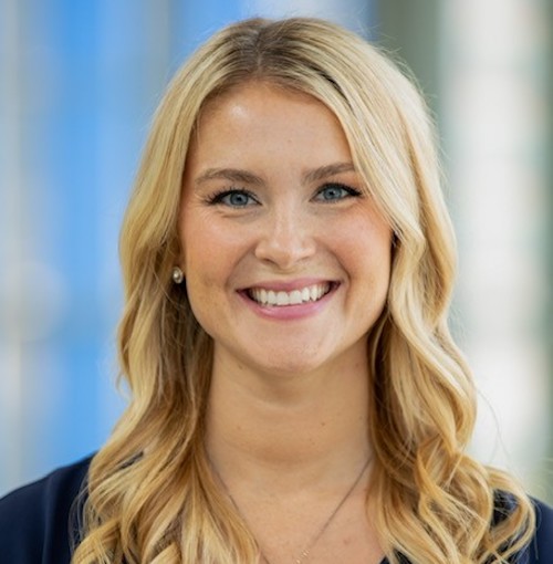 A woman with wavy blonde hair in a blue shirt smiles at the camera