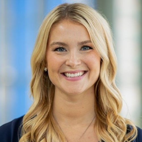 A woman with wavy blonde hair in a blue shirt smiles at the camera