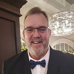 A man, Chuck Kelly, smiles in front of a chandelier. Image by Chuck Kelly.