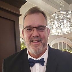 A man, Chuck Kelly, smiles in front of a chandelier. Image by Chuck Kelly.
