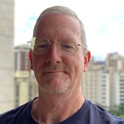 A man, Chuck Ross, smiles against a city skyline. Image by Chuck Ross.