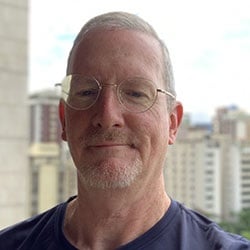 A man, Chuck Ross, smiles against a city skyline. Image by Chuck Ross.