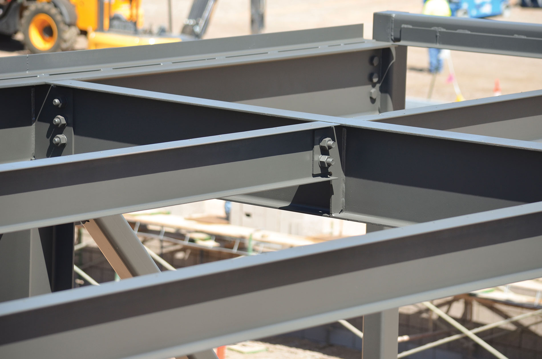 Metal bars bolted together and construction equipment in the background. Image by The Weitz Co.