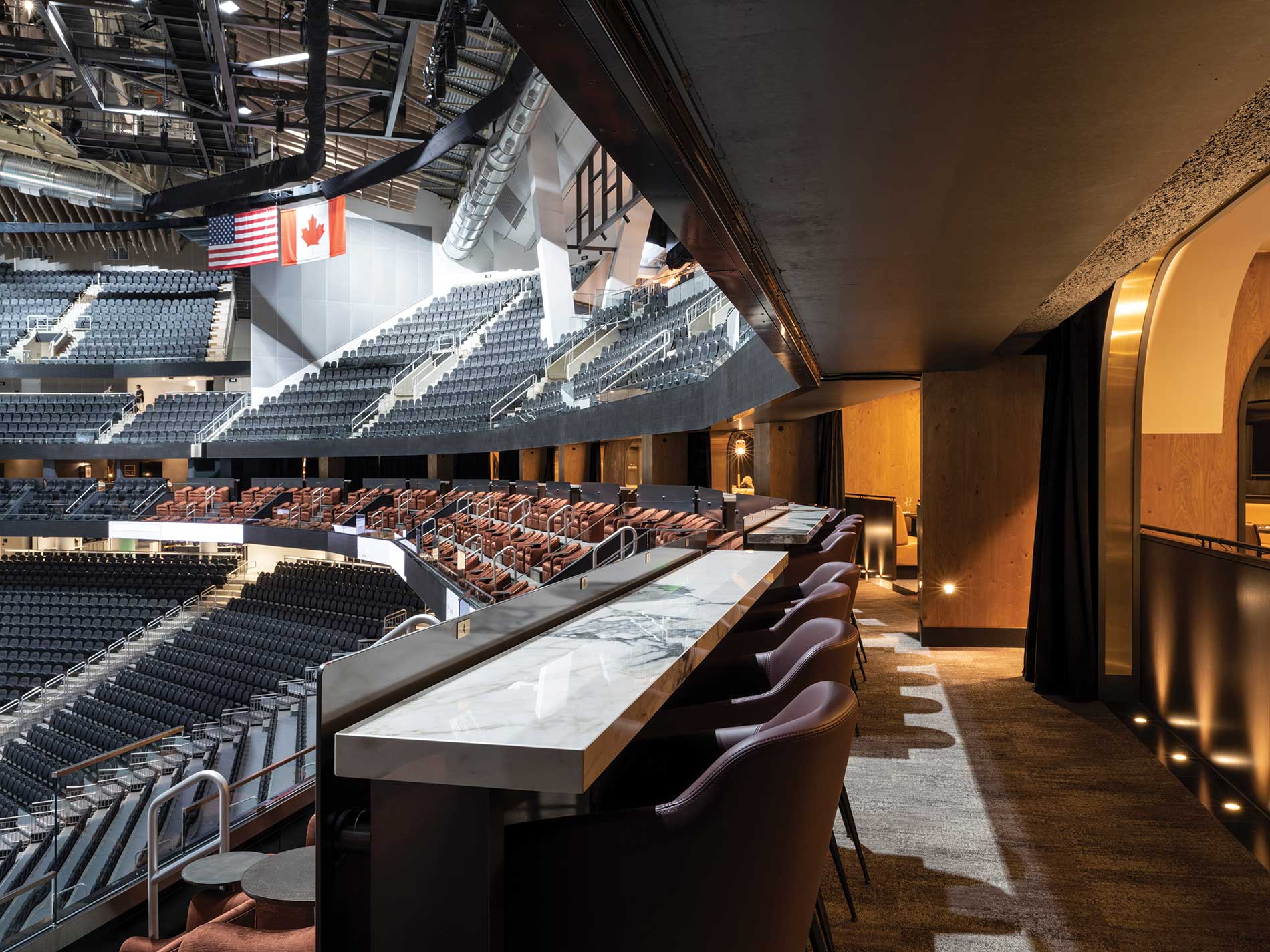 Arena interior with stadium seating and a row of lit, marble countertops with leather barstools. Image by Alex Fradkin Photography.