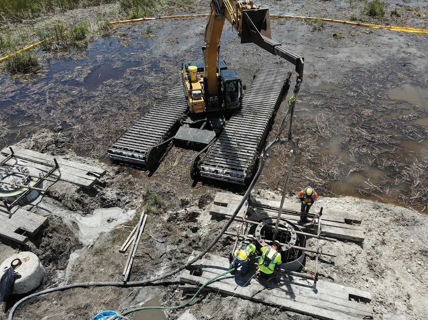 Workers on concrete platforms next to a CAT crane in muddy water. Image by Aldridge Electric.