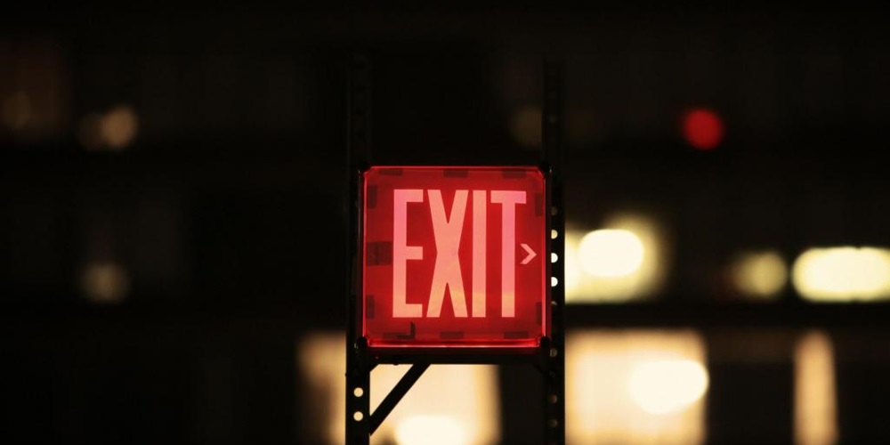 Red Exit sign against a black background with lights.