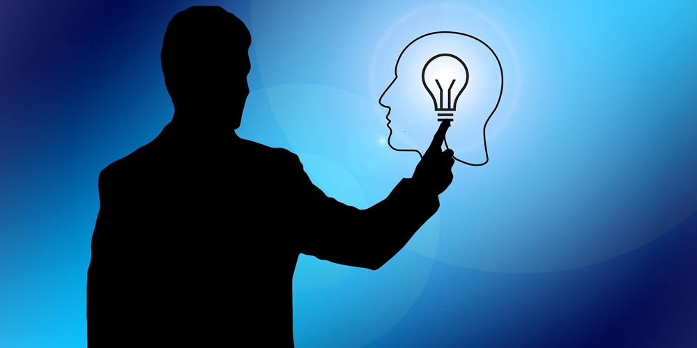 A backlit man touches an outline of a man's head with a lit lightbulb in it