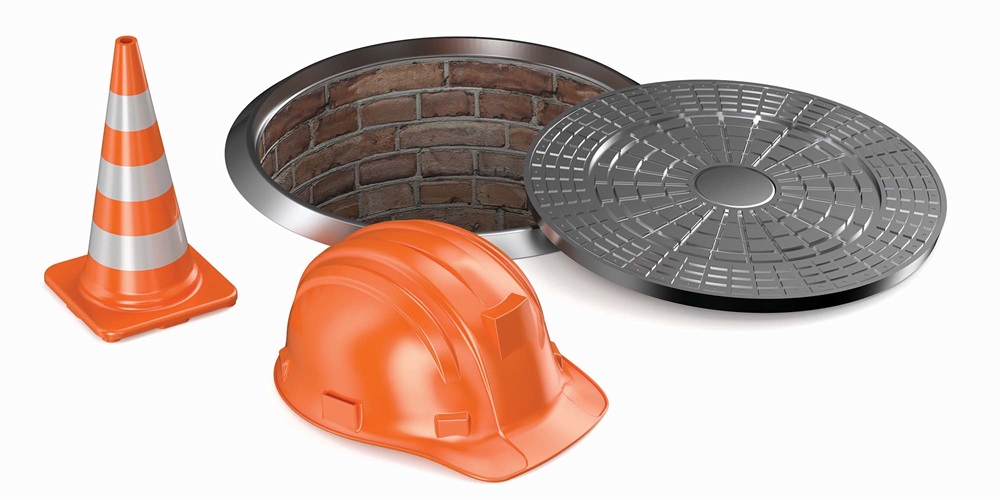A hard hat, traffic corner and a manhole cover next to an open manhole. Image by Getty Images / AlexLMX.