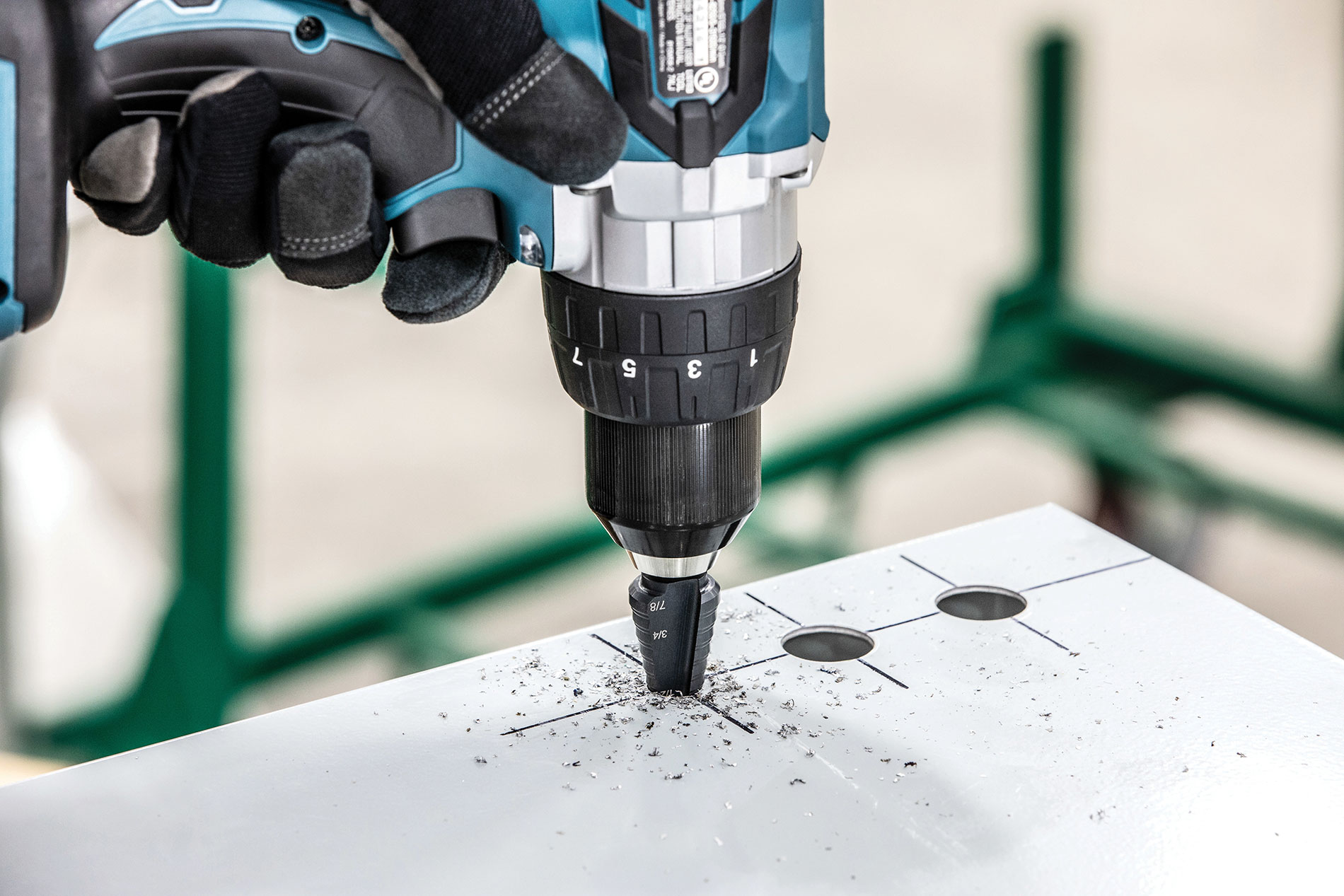 Gloved hand using multistep bit in drill. Image by www.greenlee.com.