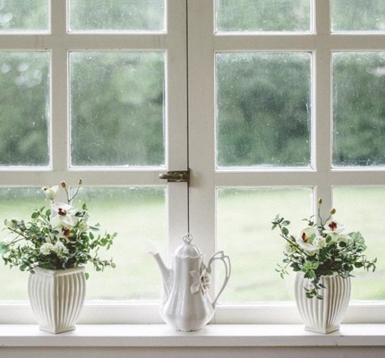 Three white vases with greenery in front of a white window and lawn.