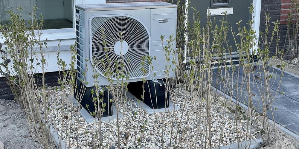 Heat pump in a gravel bed outside a brick building.