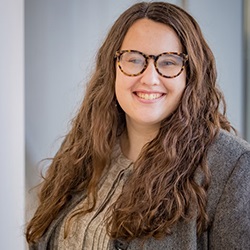 A woman, Holly Sauer, smiles in front of a gray background.