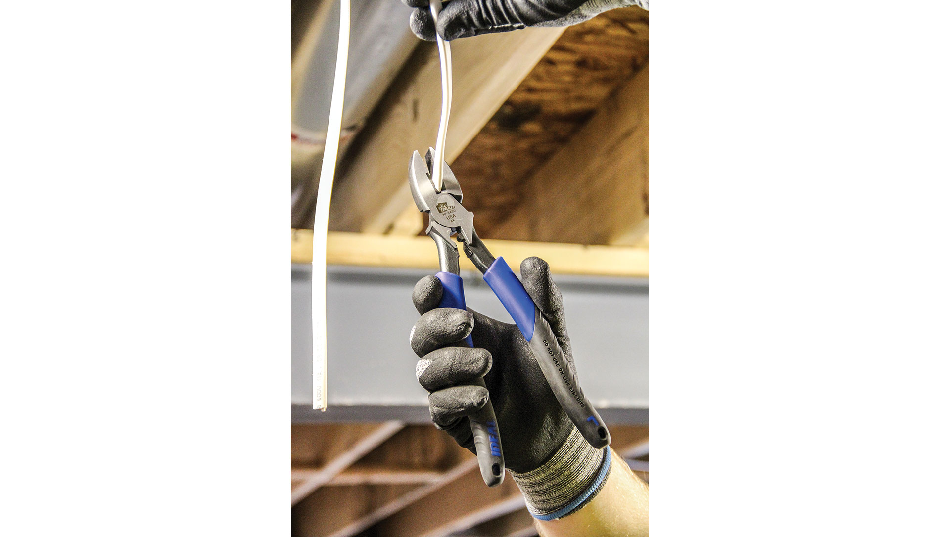 A gloved hand uses a pair of blue and gray lineman’s pliers. Image by Ideal Industries.