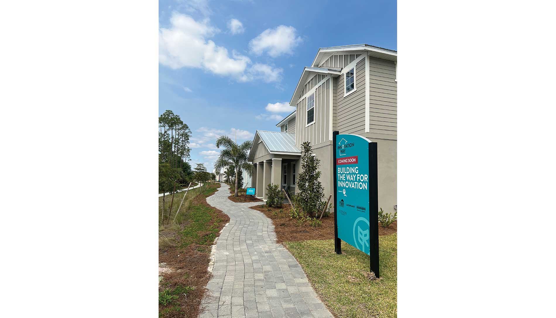 A two-story home next to trees, a concrete path, and a sign that reads,