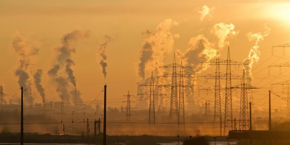 Plumes of smoke and transmission towers against a sunset. Image by Pixabay.