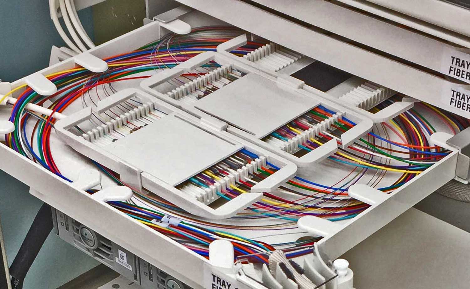 A pedestal splice tray showing 24-fiber cables with color-coded 250-micron buffer fibers on the left and 900-micron buffer pigtails on the right, demonstrating the continuity achieved through matching fiber colors.