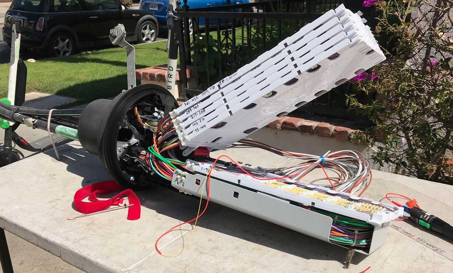Outdoor splice tray with color-coded buffer tubes coiled beneath the trays, illustrating the use of fiber optic color codes for managing and identifying 432 splices across six trays.
