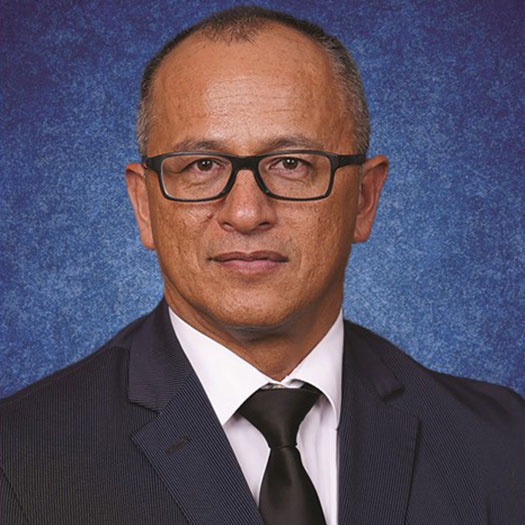 A man with short graying hair wearing glasses and a suit and tie, against a blue background