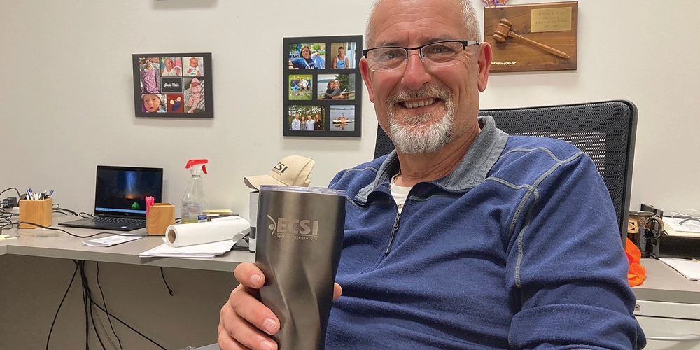 A man holds a thermos at a desk and smiles. Image by Jerry Hein.