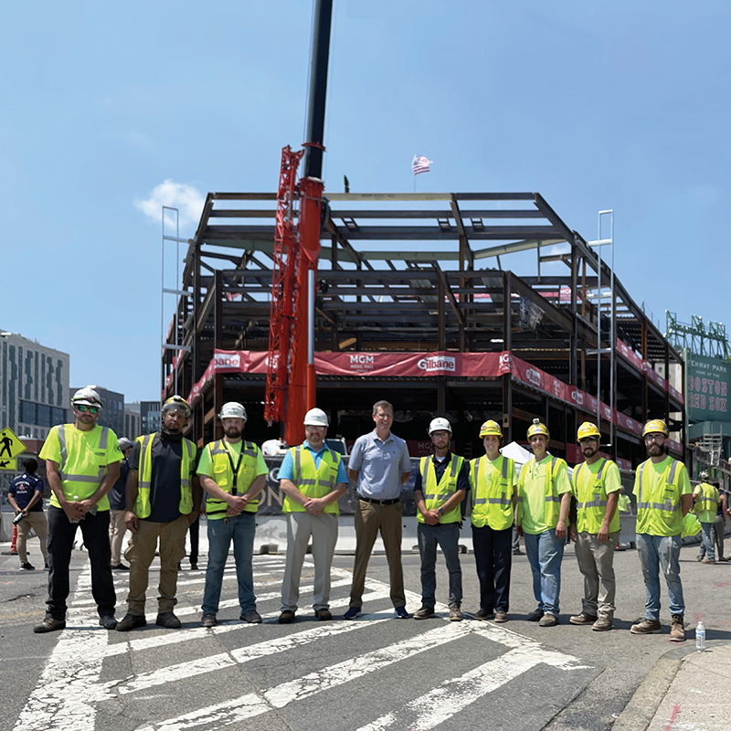Team members from Gaston Electrical pose with Sam Kennedy, president and CEO of the Boston Red Sox, in front of the new building skeleton for the MGM Music Hall at Fenway. Photo by Gaston Electrical.