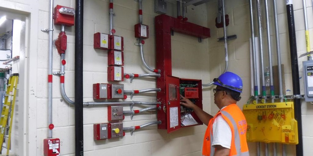 A worker looks at a fire alarm system in a cinderblock building. Image by MTA Capital Construction Mega Projects / Creative Commons Attribution 2.0 Generic license.