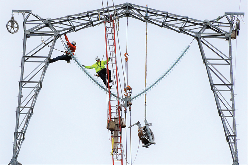 Lineworkers from Wilson Construction Co. hanging from a metal transmission tower during construction of the Great Northern Transmission Line
