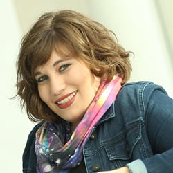 A woman, Marlena Chertock, smiles in front of a tan background. Image by Marlena Chertock.